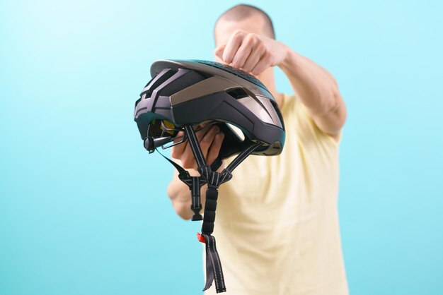 The man holds a bicycle helmet and knocks on it on a blue\
background equipment security biker adult lifestyle confidence\
standing transportation cycling head male security