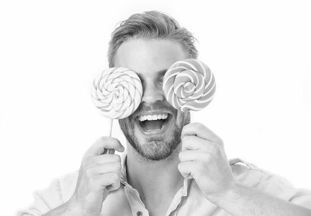 Man holds big lollipops on eyes as eyeglasses Sweet tooth concept Guy on smiling face holds two giant colorful lollipops in hands isolated on white background Man with bristle likes sweets