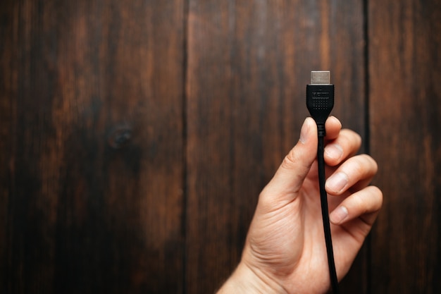 A man holds black HDMI cable in his hands on a dark wooden background