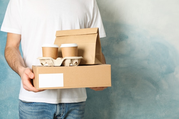 Man holds blank box, coffee cups and paper package indoor, space for text