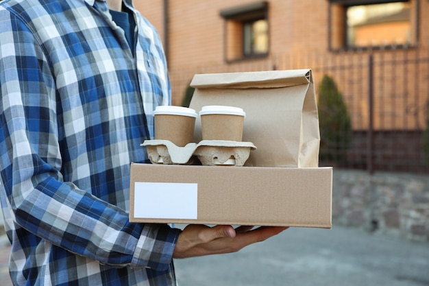 Man holds blank box, coffee cups and paper package outdoor