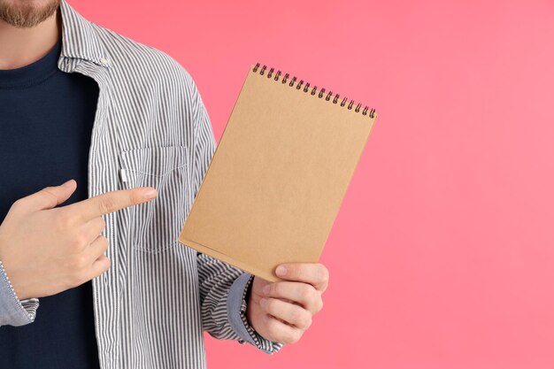 Man holds blank notebook on pink background
