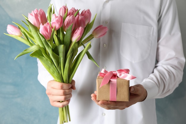 Man holds bouquet of pink tulips and gift on blue, close up