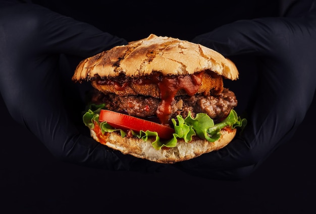 Man holds burger with nugget and cutlet in hands in black gloves