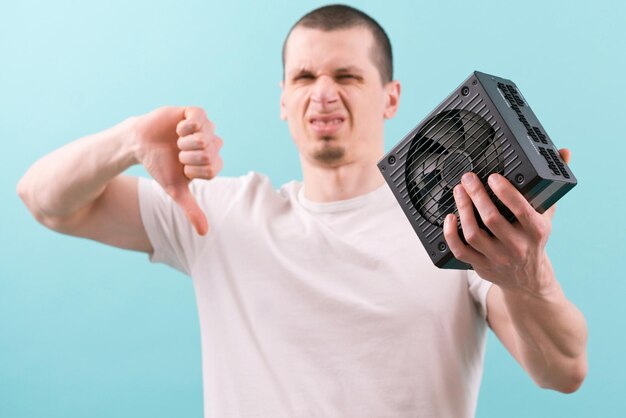 A man holds a computer power supply and shows thumbs down on a blue background Energy Cable Cooler Disagree Metal Disapprove Control Failure Device Sign Isolated Electrical Fan Finger