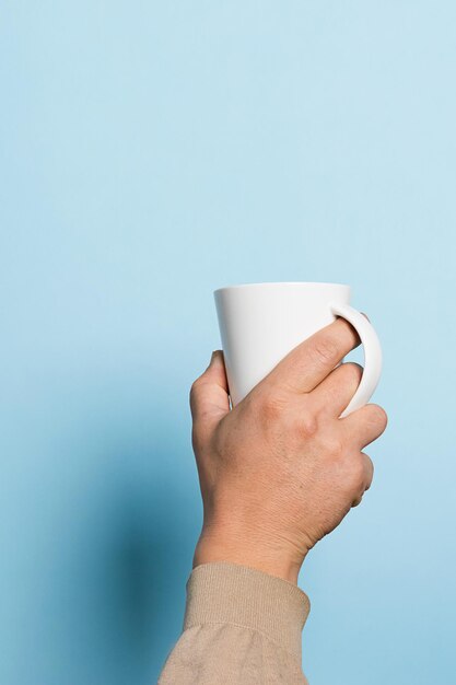 A man holds a cup of coffee or tea drink high in his hand a\
blue background food drink concept copy space