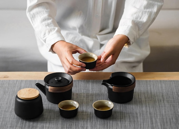 A man holds a cup of tea in front of four small cups