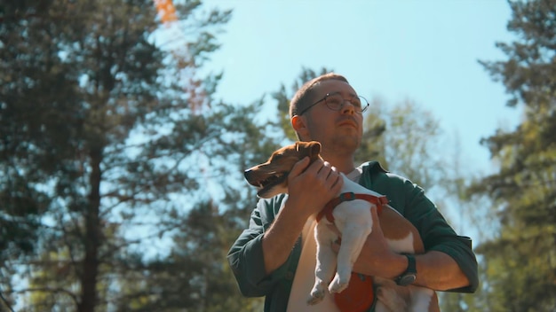 Мужчина держит собаку в руках в парке. Кадр. Красивый мужчина с собакой в руках гуляет в лету в лесу.