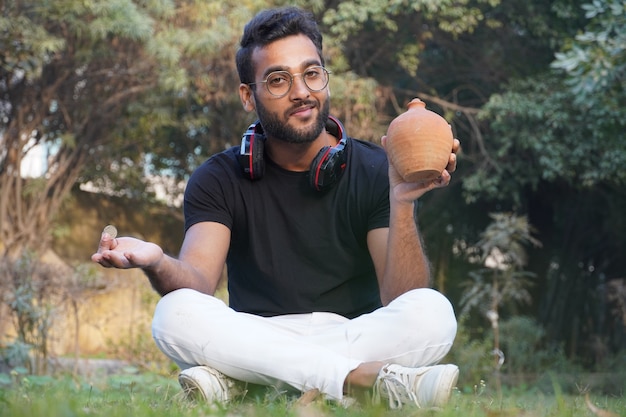 A man holds an earphone on his shoulder and holds the piggy bank in his hand