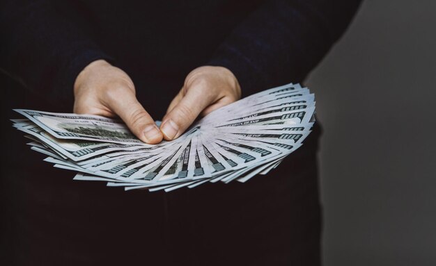 A man holds a fan of 100 dollar bills in his hands