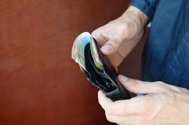 Мужчина держит в руках черный кожаный кошелек с украинскими деньгами или вора, который украл полный кошелек денег