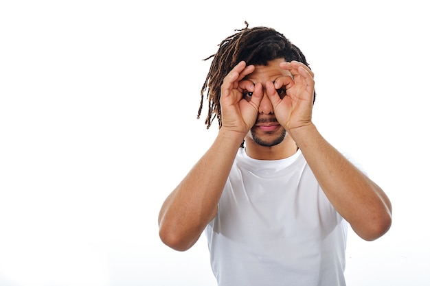 Man holds hands near eyes and pretends to look through binoculars while standing on an isolated background.