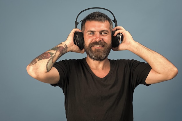 Man holds headphones on blue background Dj with beard