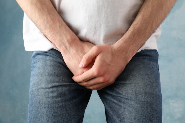 Man holds his crotch on blue, close up