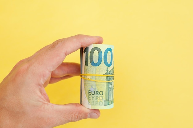 The man holds in his hand money roll of euro banknotes with yellow rubber band on yellow background