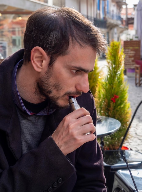 A man holds in his hand and smokes an electronic cigarette VAPE and releases clouds of steam smoke