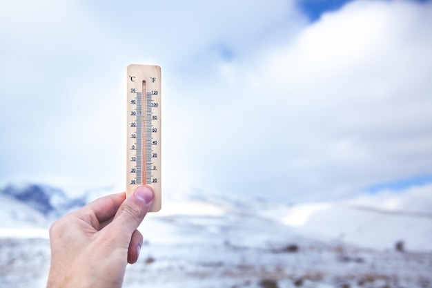 A man holds in his hand a snow thermometer showing the temperature