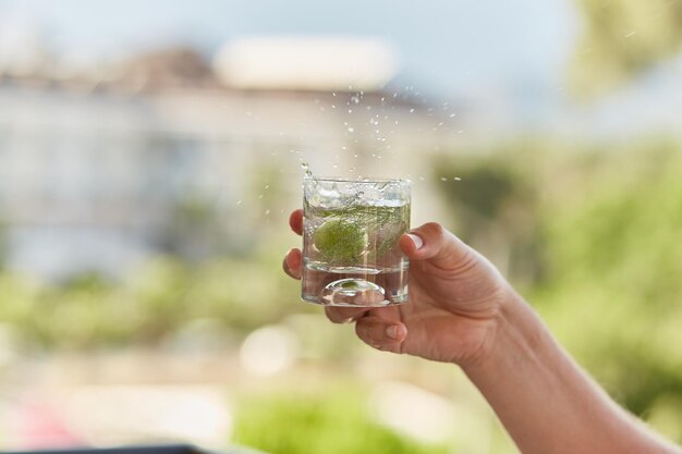 L'uomo tiene tra le mani un bicchiere di cocktail fatto in casa di seltz duro con erbe di fronte alle montagne