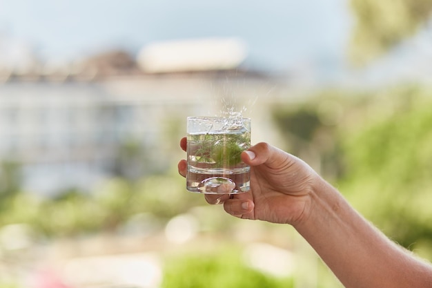 Man holds in his hands a glass of homemade cocktail with antioxidant herbs in front of mountains