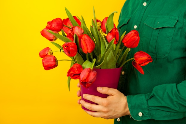 男は彼の手にチューリップの花束が付いている花瓶を保持しています