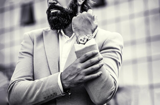 Фото Мужчина держит часы портрет успешного бизнесмена в деловом костюме с часами на фоне города черно-белый