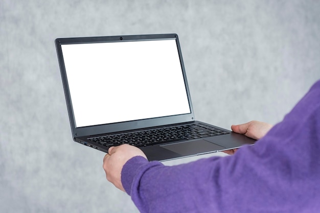 Man holds a laptop in his hands with a mockup of a white screen on a light background