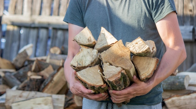 A man holds a lot of chopped firewood in his hands