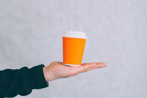 A man holds a mock-up of a paper cup for coffee and tea on a light.