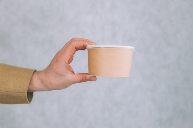 A man holds a mock-up of a paper cup for soup, coffee and tea on a light.