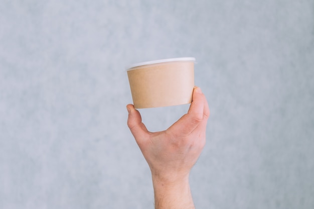 A man holds a mock-up of a paper cup for soup, coffee and tea on a light.