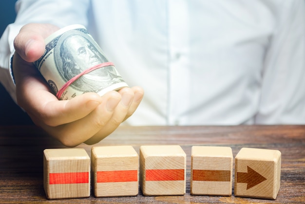 Man holds money above of blocks of red arrow Financing and investing in completion of a business