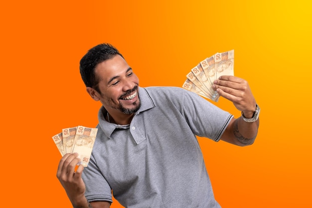 Man holds money Brazilian money in both hands happy smile on orange background