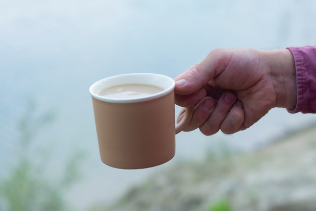 Photo man holds a mug with coffee in his hands on the background of nature.