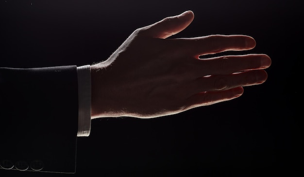 A man holds out his hand for a handshake highlighted on a black\
background