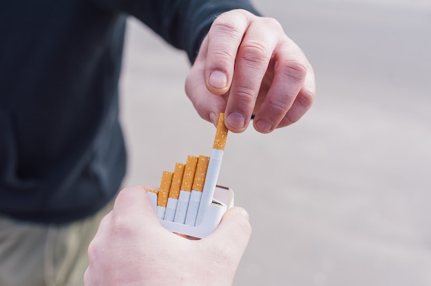 The man holds a pack of cigarettes and offers it to the man.