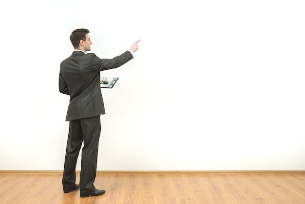 The man holds papers and gestures on the white wall background