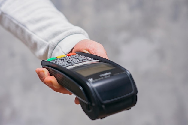 Man holds a payment terminal for cashless payments in his hand\
against the background of a concrete wall