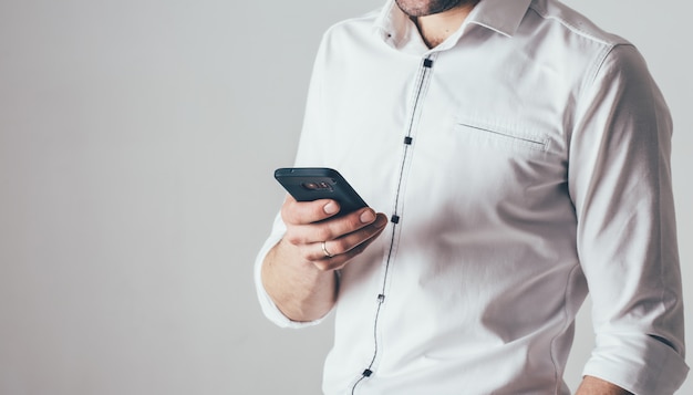 A man holds a phone in his hand. He is dressed in a white shirt