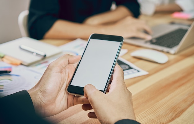 The man holds the phone on a wooden desk in the office