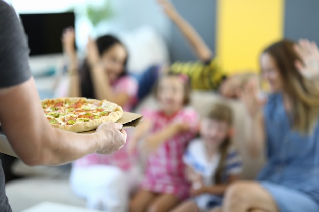 Man holds pizza in his hands, rejoicing children and adults.