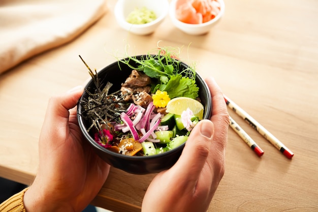 Un uomo tiene in mano un'insalata di poke con carne di manzo in una ciotola ingredienti concetto di insalata asiatica di manzo