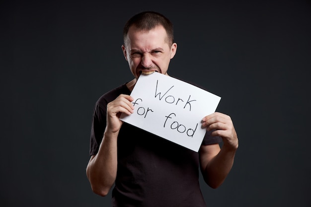 L'uomo tiene in mano un foglio di carta per poster con la scritta i work for food. sorriso e gioia, posto per il testo, copia spazio