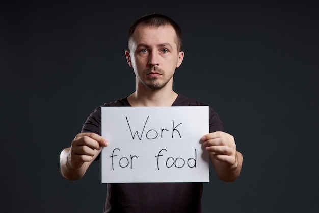 Мужчина держит в руках лист плаката с надписью «Я работаю за еду». Улыбка и радость, место для текста, место для текста