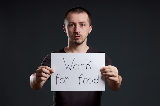 Man holds a poster paper sheet in his hands with the inscription I work for food. Smile and joy, place for text, copy space