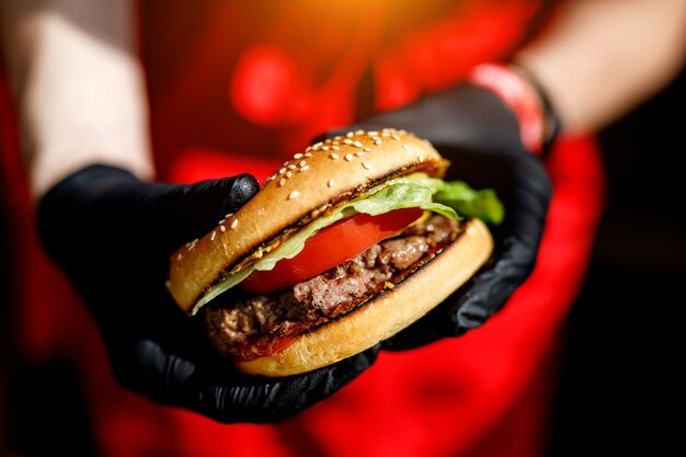 Man holds ready tasty burger in hands in black gloves.