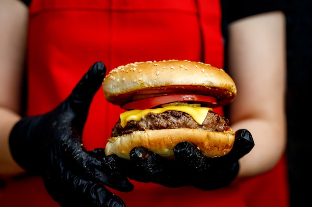 Man holds ready tasty burger in hands in black gloves.