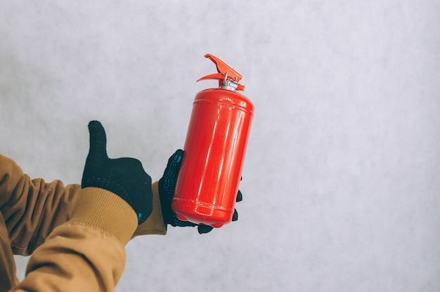 A man holds a red fire extinguisher in his hands on a white.