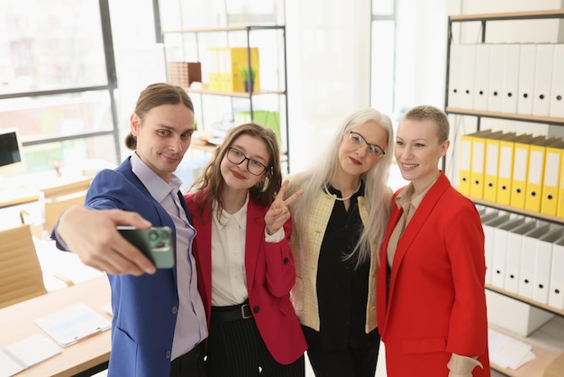 Man holds smartphone taking selfie with female colleagues in office happy employees in formal