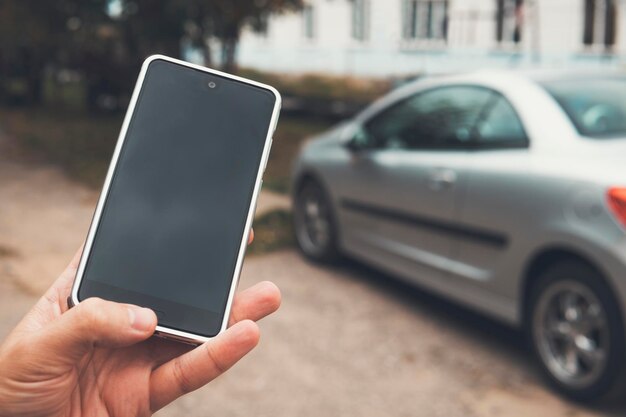 Photo man holds a smartphone with a black screen at a blurred car background person uses mobile to unlock