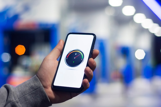 A man holds a smartphone with a digital fuel meter on the screen